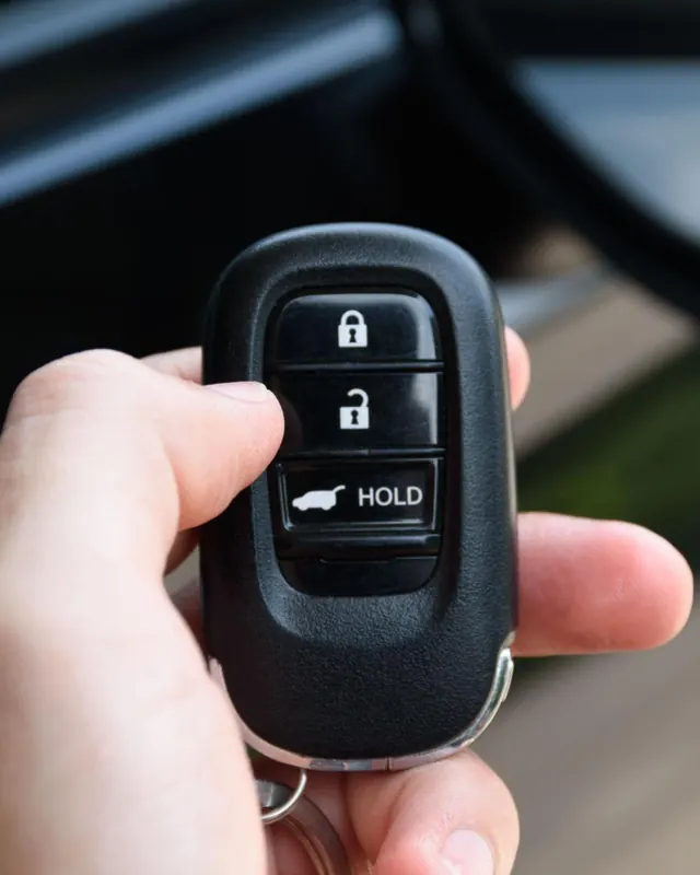 Mão segurando chave de carro com controle ao lado do veículo